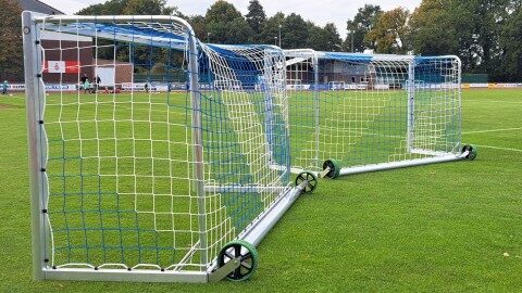 Aluminium Fußballtor 3×1,6 m Safety mit Kippschutz und Vollgummirädern auf Naturrasen vor Vereinstribüne, Seitenansicht