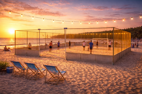 Beach Soccer Court für Events und Turniere, mobil, Aluminium-Bandensystem, Soccer Eventsport Beach Soccer Court bei Sonnenuntergang am Strand, Spieler auf Sandfeld, umlaufendes goldenes Netz, Lichterkette, Liegestühle im Vordergrund