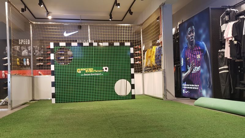 Torwand mieten mit individuellem Branding für Messen und Events, Soccer Eventsport Torwand mit grünem Kunstrasenbezug und Soccer-Eventsport-Branding auf Messestand, dahinter Fußballtor, Innenaufnahme