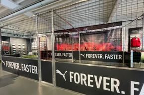 Werbebanden mieten mit individuellem Branding für Sponsoren und Marketingauftritte, Soccer Eventsport Innenansicht eines Soccer Courts mit vollflächigem Puma-Branding auf den Banden, Netz und Schaufenster im Hintergrund