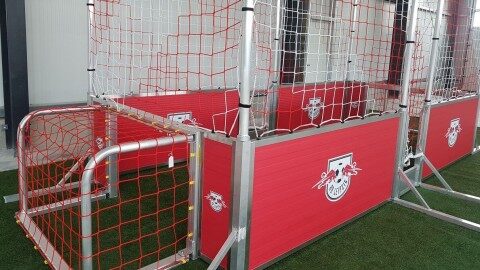 Speedkick-Anlage mit zwei Aluminiumtoren und umlaufendem rotem Bandensystem mit RB-Leipzig-Branding, aufgestellt auf Kunstrasen in einer Halle, Frontalansicht