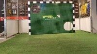 Torwand mieten mit individuellem Branding für Messen und Events, Soccer Eventsport Torwand mit grünem Kunstrasenbezug und Soccer-Eventsport-Branding auf Messestand, dahinter Fußballtor, Innenaufnahme