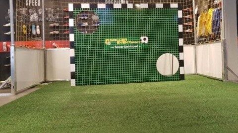 Torwand mit grünem Kunstrasenbezug und Soccer-Eventsport-Branding auf Messestand, dahinter Fußballtor, Innenaufnahme