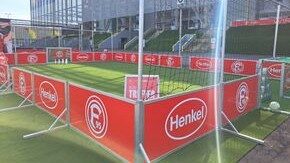 Speedkick-Anlage mit umlaufendem rotem Bandensystem und Henkel- sowie Fortuna-Düsseldorf-Branding, aufgestellt auf Kunstrasen vor Stadion, Außenansicht von schräg oben
