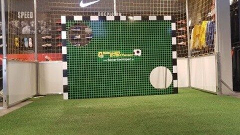 Torwand mit grünem Kunstrasenbezug und Soccer-Eventsport-Branding auf Messestand, dahinter Fußballtor, Innenaufnahme