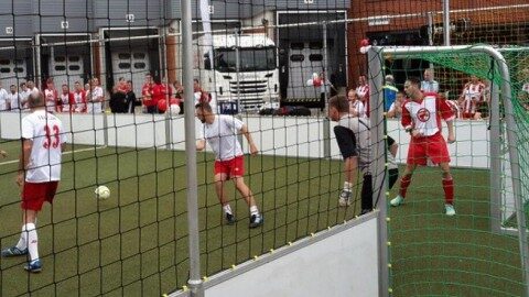 Speedkick-Anlage mit umlaufendem rotem Bandensystem und Henkel- sowie Fortuna-Düsseldorf-Branding, aufgestellt auf Kunstrasen vor Stadion, Außenansicht von schräg oben